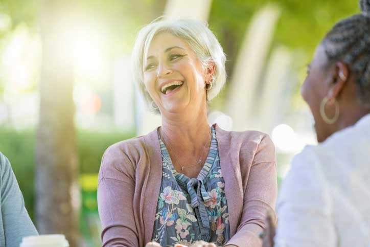 iStock-1043661782 a senior woman sitting outside and laughing with friends
