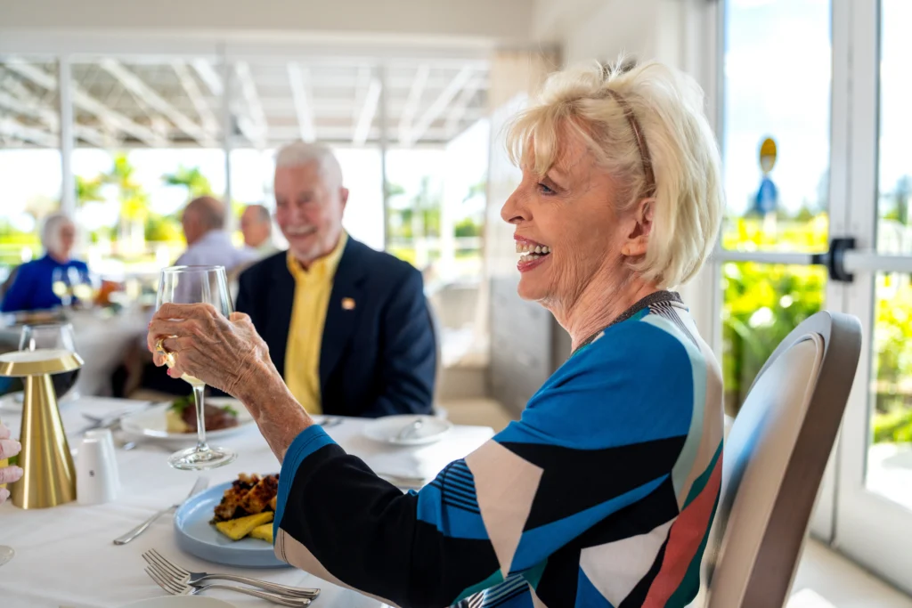 An elderly couple, residents of Amavida in Fort Myers, FL, smiling and toasting during lunch.