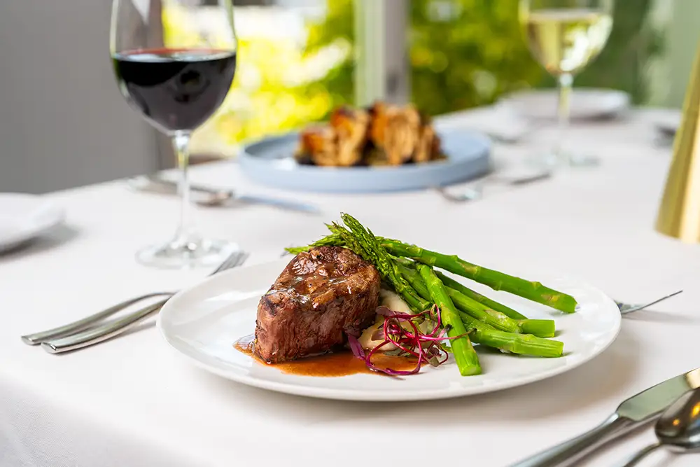 A detailed close-up of a steak and asparagus dish served in a bright dining room for Amavida residents.
