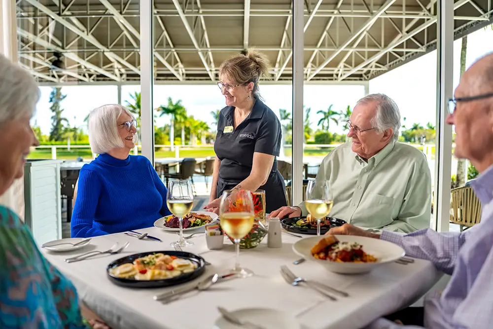 Seniors at Amavida enjoy a dining experience at a white tablecloth table, with a staff member attending to them.